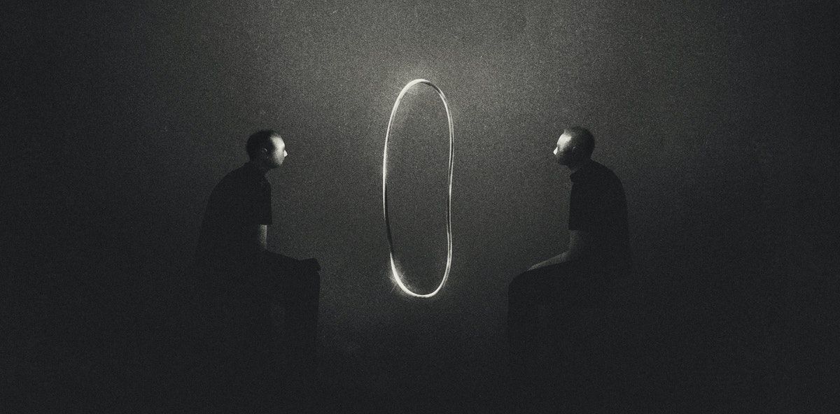 Ibrahim Rayintakath's illustration for 'The year you healed your therapist'. Shows two men sitting facing eath other in a dark space, separated by a shimmering oval object that gives the impression of a mirror.